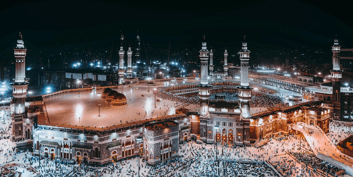 Night view of the Masjid an Nabawi in Mecca with numerous people gathered around the Kaaba.