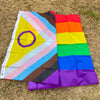 A vibrant Pride rainbow flag banner displayed outdoors on dry grass.