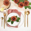 A flat lay of artificial real touch foam roses in various shades of terracotta and green on a white background.