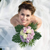 A smiling woman wearing a white dress holds a bouquet of purple and white artificial tropical palm leaves for party decor.