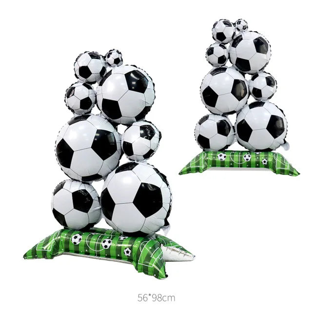 A stack of white and black soccer ball foil balloons on a green striped base.