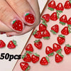 A close-up of red strawberry shaped 3D resin ladybug nail art charms arranged on a pink background.
