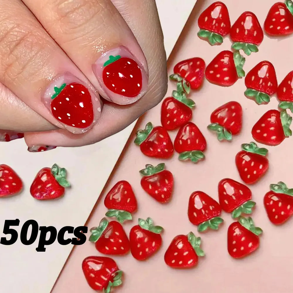 A close-up of red strawberry shaped 3D resin ladybug nail art charms arranged on a pink background.
