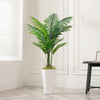Artificial palm tree floor decor in a white pot displayed indoors next to a window.