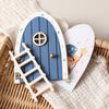 A wooden fairy elf door miniature decoration featuring a blue arched door and a wooden ladder.