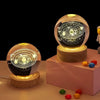A set of three 3D laser engraved crystal ball decorations with internal light displays on a pink surface.