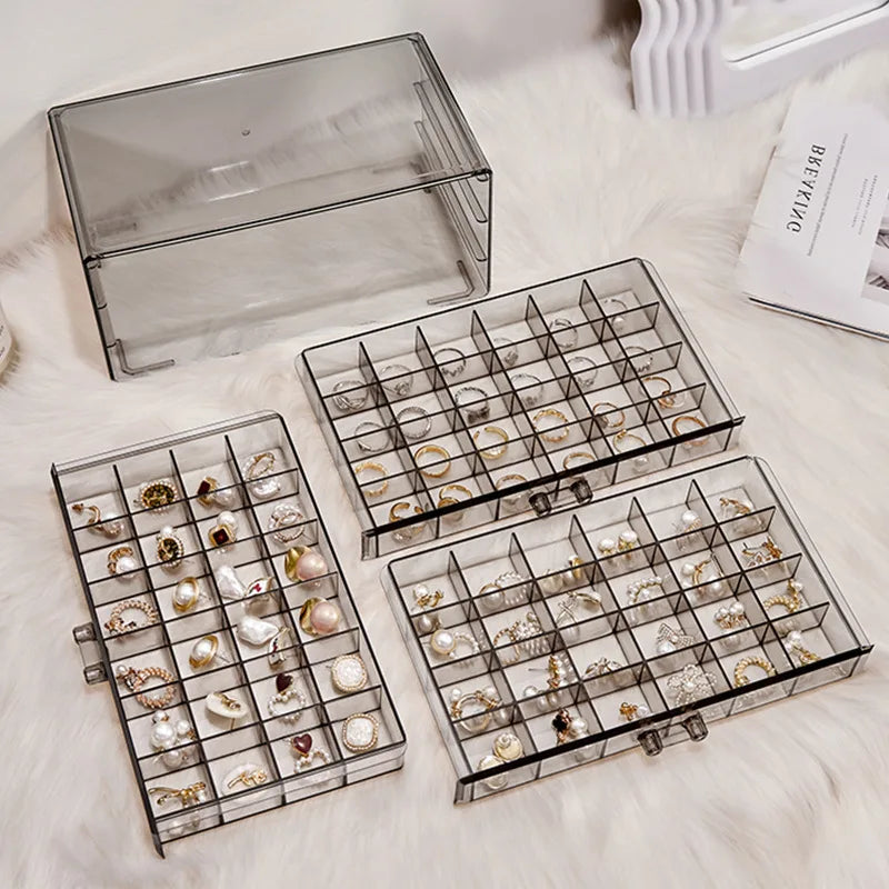 Clear acrylic jewelry organizer with three drawers displayed on a white fluffy surface.