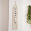 A cream-colored macrame wall hanging featuring a fringe and multiple blue evil eye pendants.