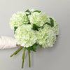 A bouquet of light green artificial hydrangea flowers with green stems and a white fabric in the background.