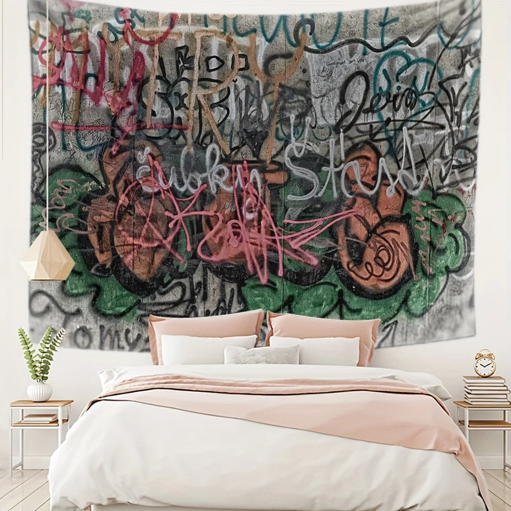 A large tapestry featuring bold urban graffiti and street art in shades of black, gray, pink, and green hanging above a bed.