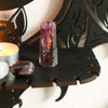 A deep purple amethyst crystal and a candle displayed on black gothic bat moon floating wall decor.