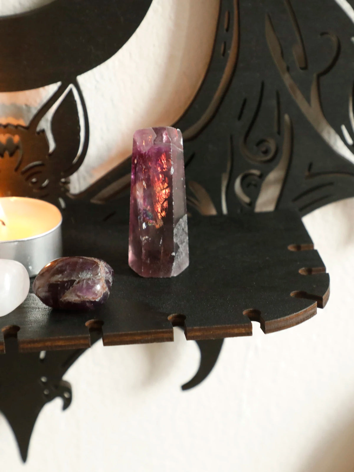 A deep purple amethyst crystal and a candle displayed on black gothic bat moon floating wall decor.