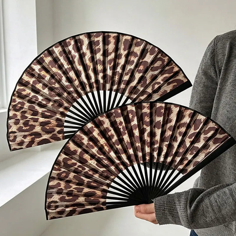 Nahaufnahme eines gefalteten, handgehaltenen Leopardenmuster-Ventilators mit braunen und schwarzen Flecken, gehalten von eine