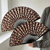 Nahaufnahme eines faltbaren Handfans mit Leopardenmuster in Braun- und Schwarztönen, gehalten von einer Person.