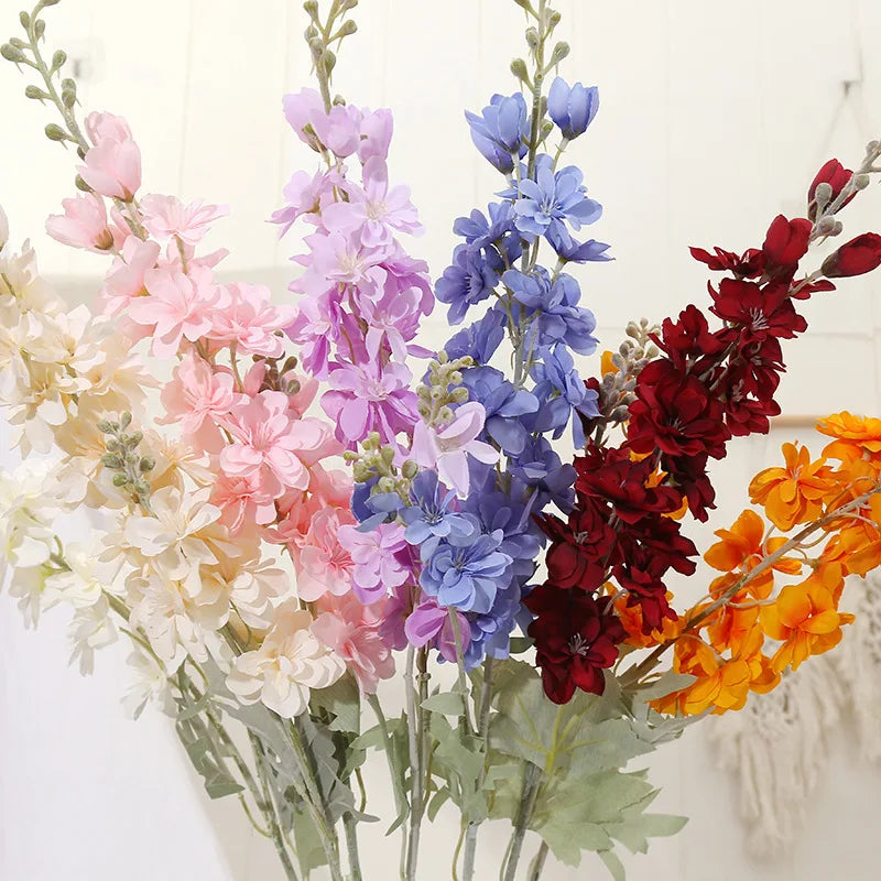 Un bouquet de fleurs artificielles de delphinium dans des tons de rose, violet, bleu et rouge.