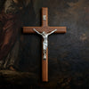 A hand-carved wooden cross with a silver crucifix mounted on a dark background.