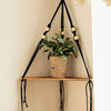 Étagère flottante en bois bohème avec porte-macramé noir tenant une plante en pot.
