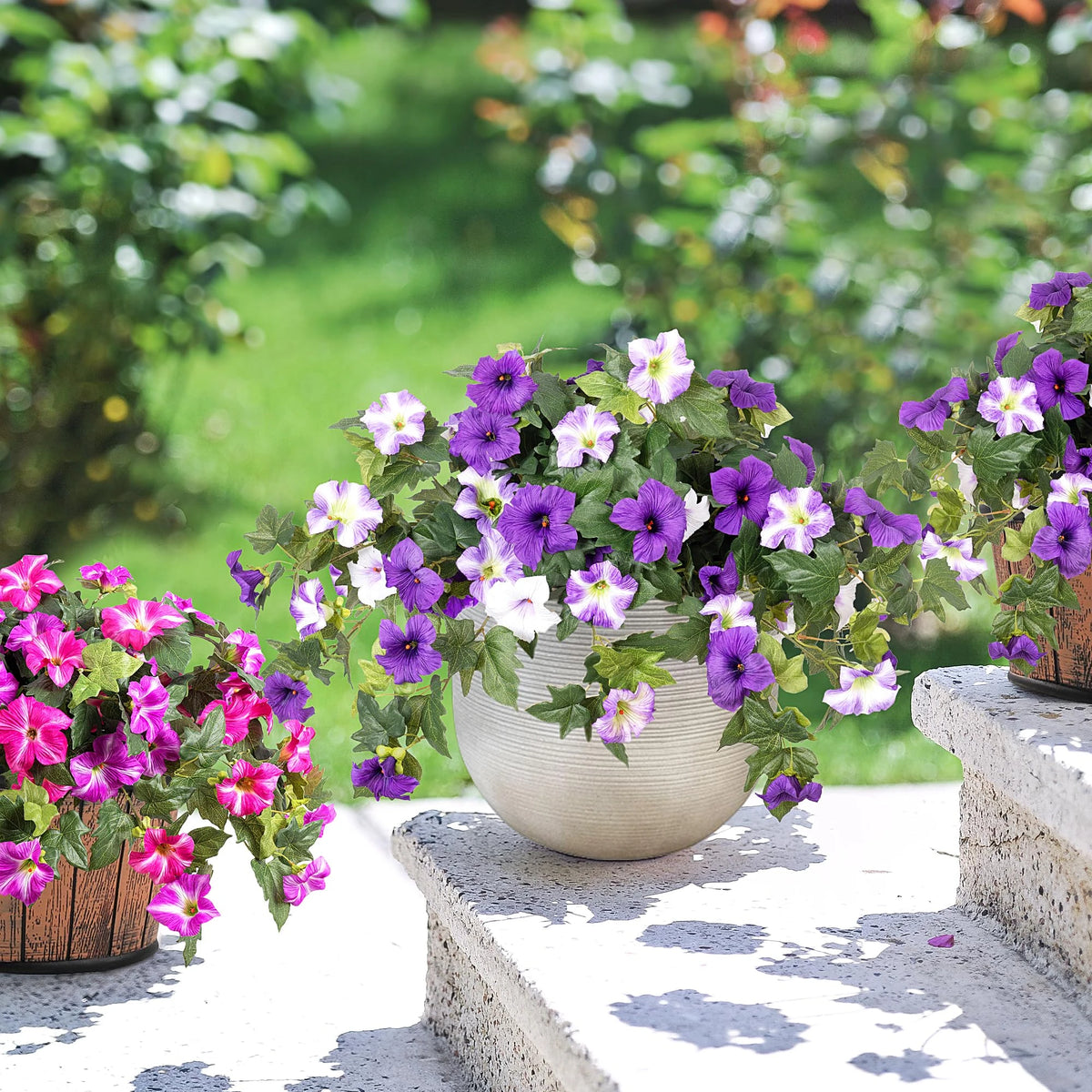 A bundle of purple and white artificial petunias displayed on a stone ledge in an outdoor garden setting.