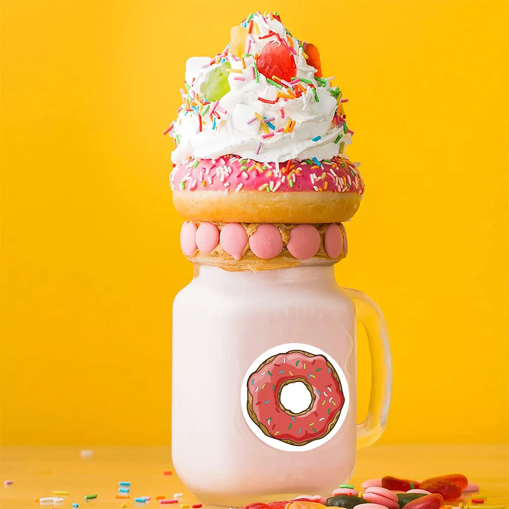 A pink milkshake glass filled with a creamy beverage, topped with whipped cream and colorful sprinkles, next to round donut l