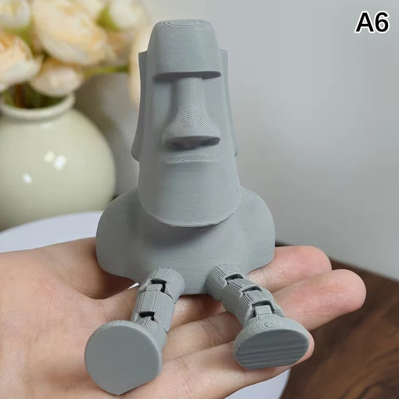 A hand holds a gray 3D printed Moai statue figurine with movable joints.