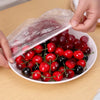 A hand is removing a clear plastic wrap from a bowl filled with various red and black cherries.