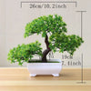 A small artificial tree bonsai decoration with green foliage planted in a white rectangular pot.