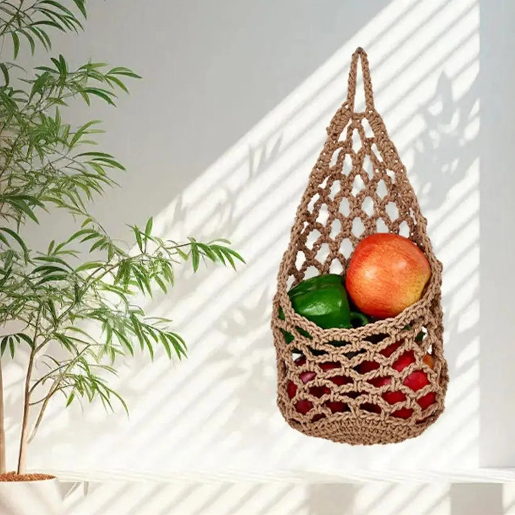 A macrame hanging storage basket filled with fresh fruits and vegetables, casting shadows on a white wall.