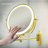 A hand is holding a round, illuminated makeup mirror with a gold frame and a light ring.