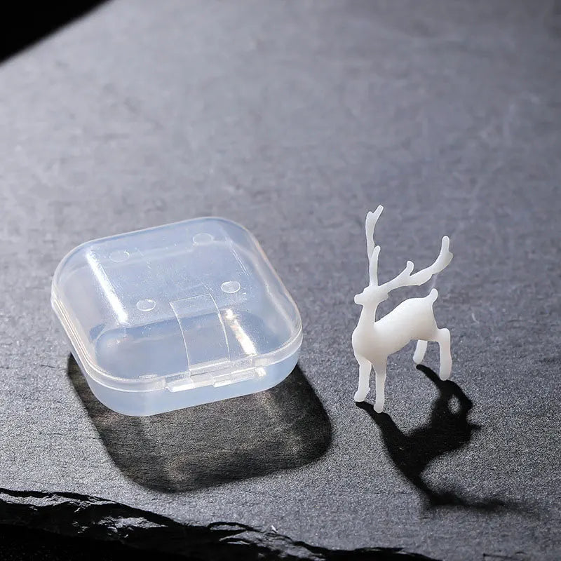 A clear plastic resin ornament shaped like a small elk or deer standing on a dark gray surface.