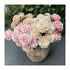 A bouquet of silk roses in shades of peach, cream, and pink arranged in a rustic vase.