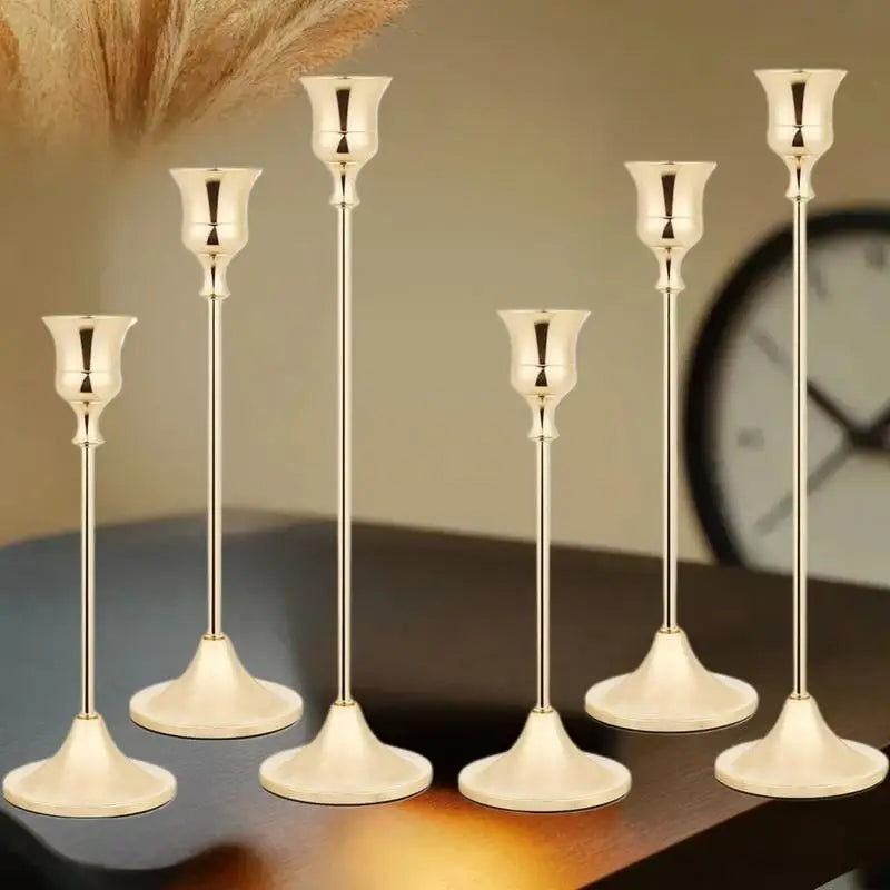 A set of three matte gold taper candle holders displayed on a dark wooden surface.