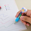A hand holds a heart-shaped multicolor ballpoint pen with a yellow bear charm over a lined sheet of paper.