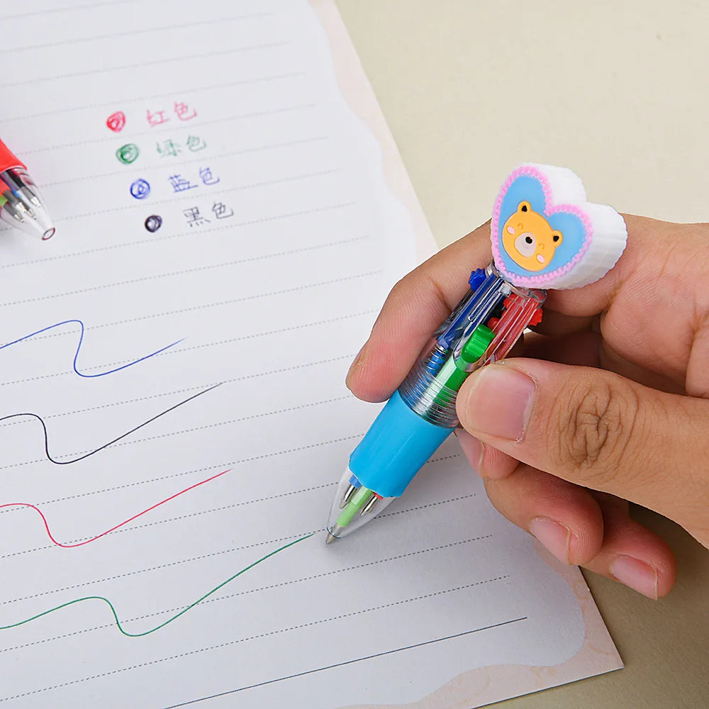A hand holds a heart-shaped multicolor ballpoint pen with a yellow bear charm over a lined sheet of paper.