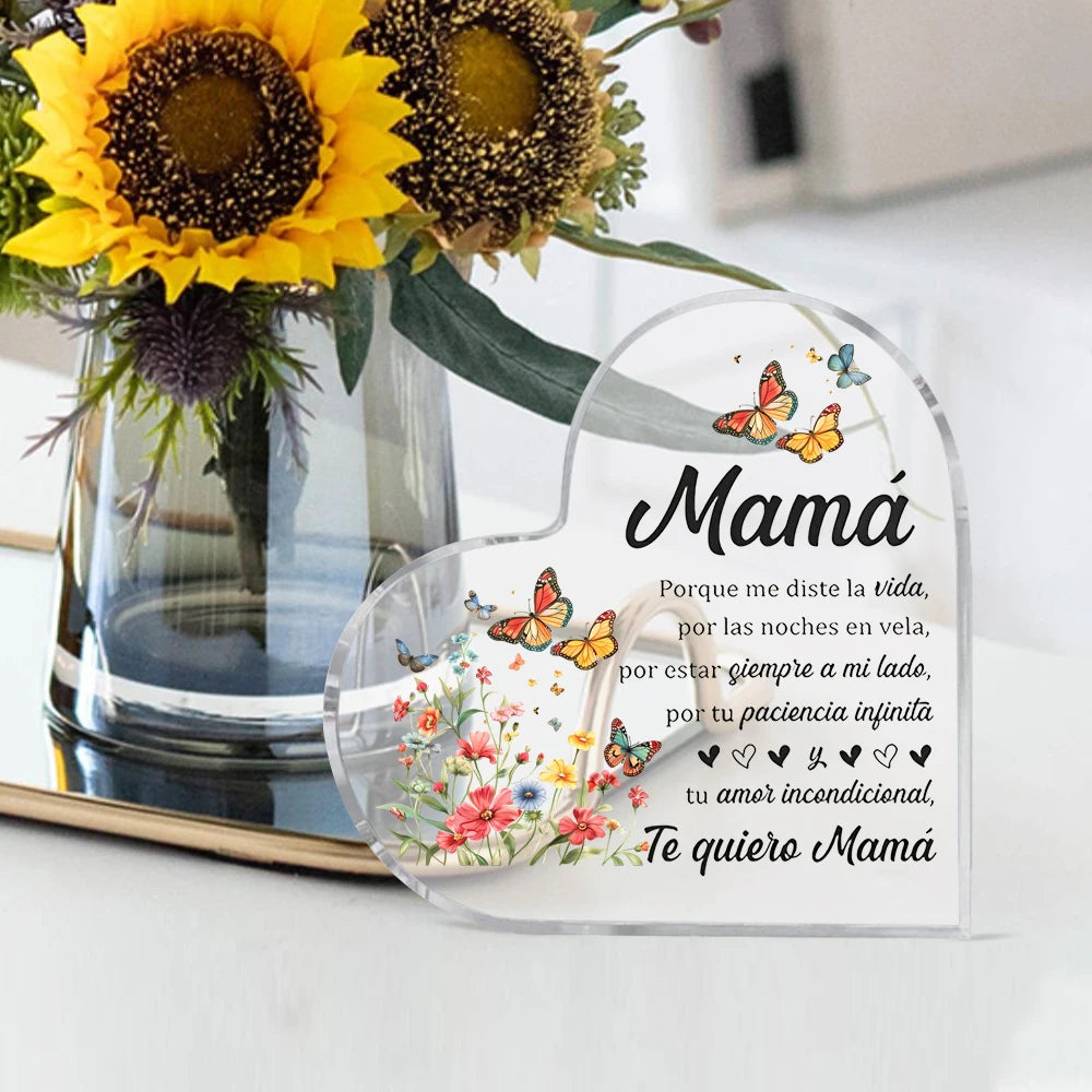 A clear heart-shaped ornament featuring floral designs and text in Spanish expressing love for Mom
