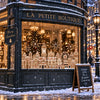 A storefront window decorated with Christmas gingerbread house window clings and snow outside.