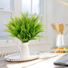 A vase filled with vibrant green artificial Boston ferns on a white tray indoors.