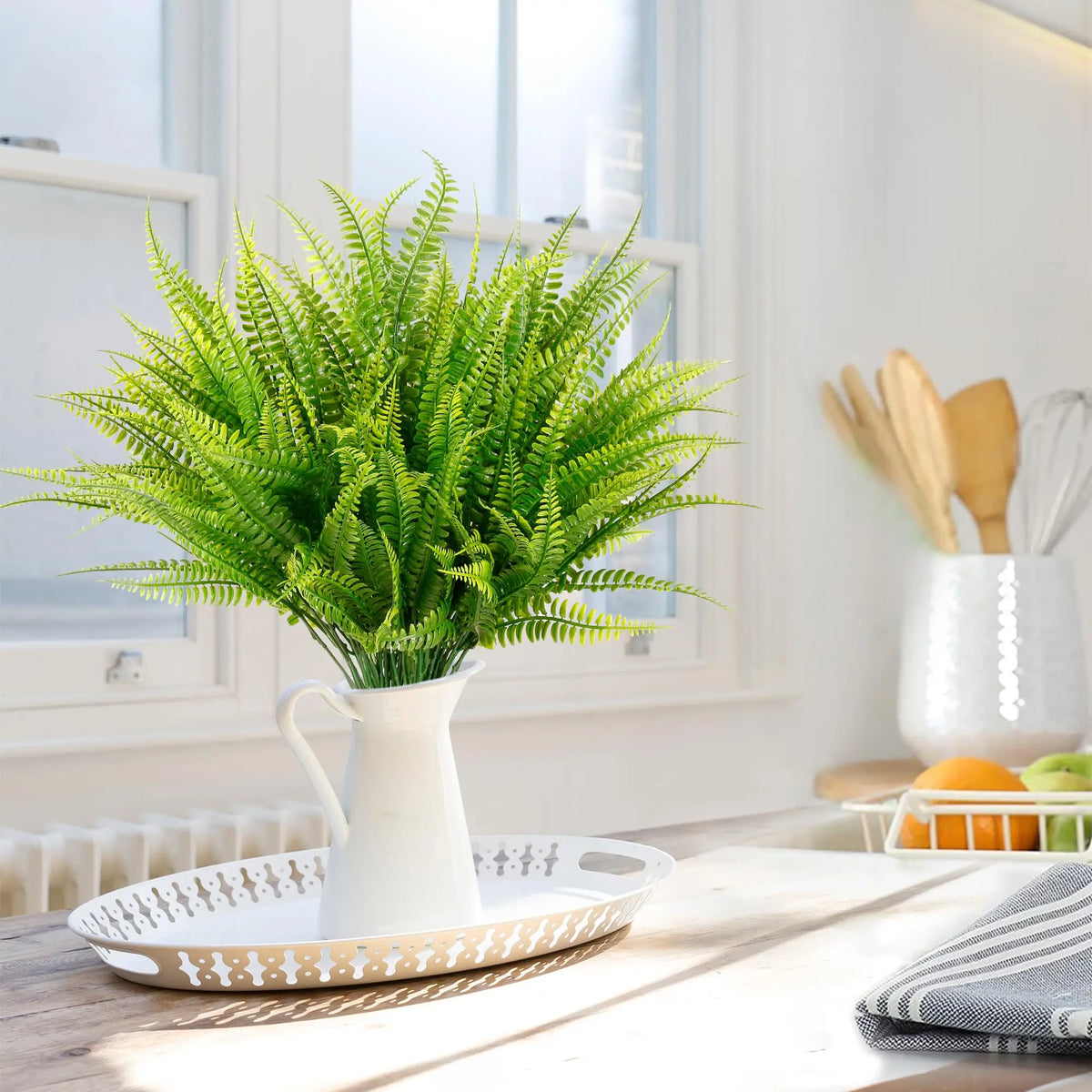 A vase filled with vibrant green artificial Boston ferns on a white tray indoors.