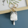 A handcrafted crochet cat keychain pendant with gray and white yarn, hanging from a gold-colored split ring.