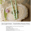 Two long-stemmed printed candles in light green with a small white flowers print displayed on a lace plate.