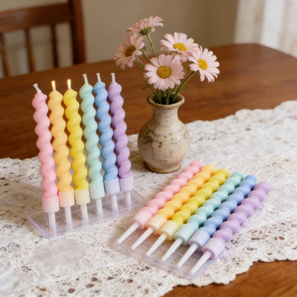 A display of spiral birthday cake candles in pink, yellow, and blue colors with star toppers on a wooden surface.