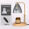 A gold-toned adjustable candle warmer lamp with a glass shade and a wooden base, next to instructions.
