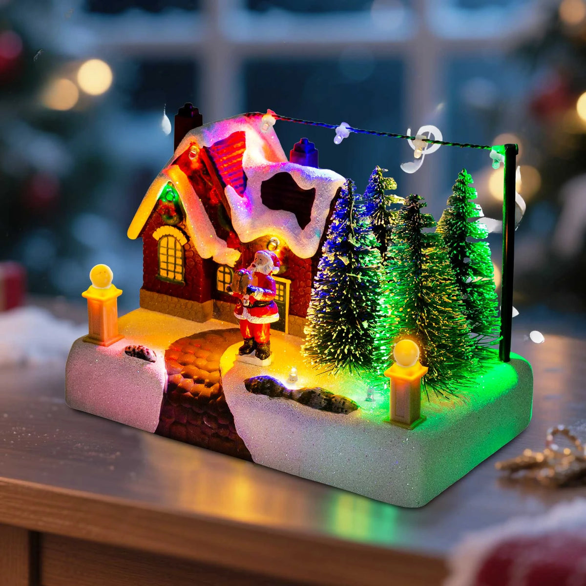 Illuminated Christmas village scene featuring a red house, Santa, and snowy evergreen trees.