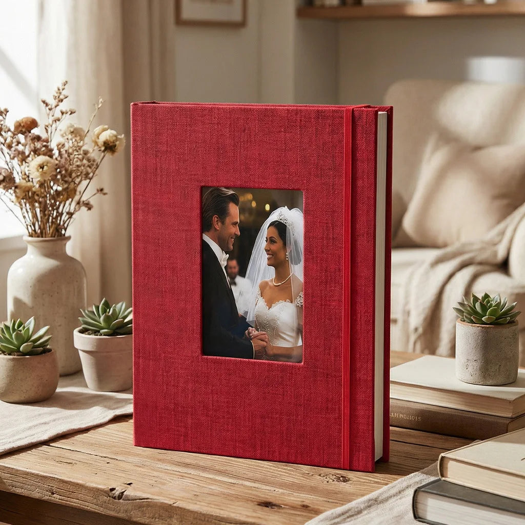 A red linen photo album with a square window displaying a portrait of a smiling couple.