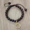 A black beaded bracelet with a gold charm featuring the zodiac symbol for Libra.