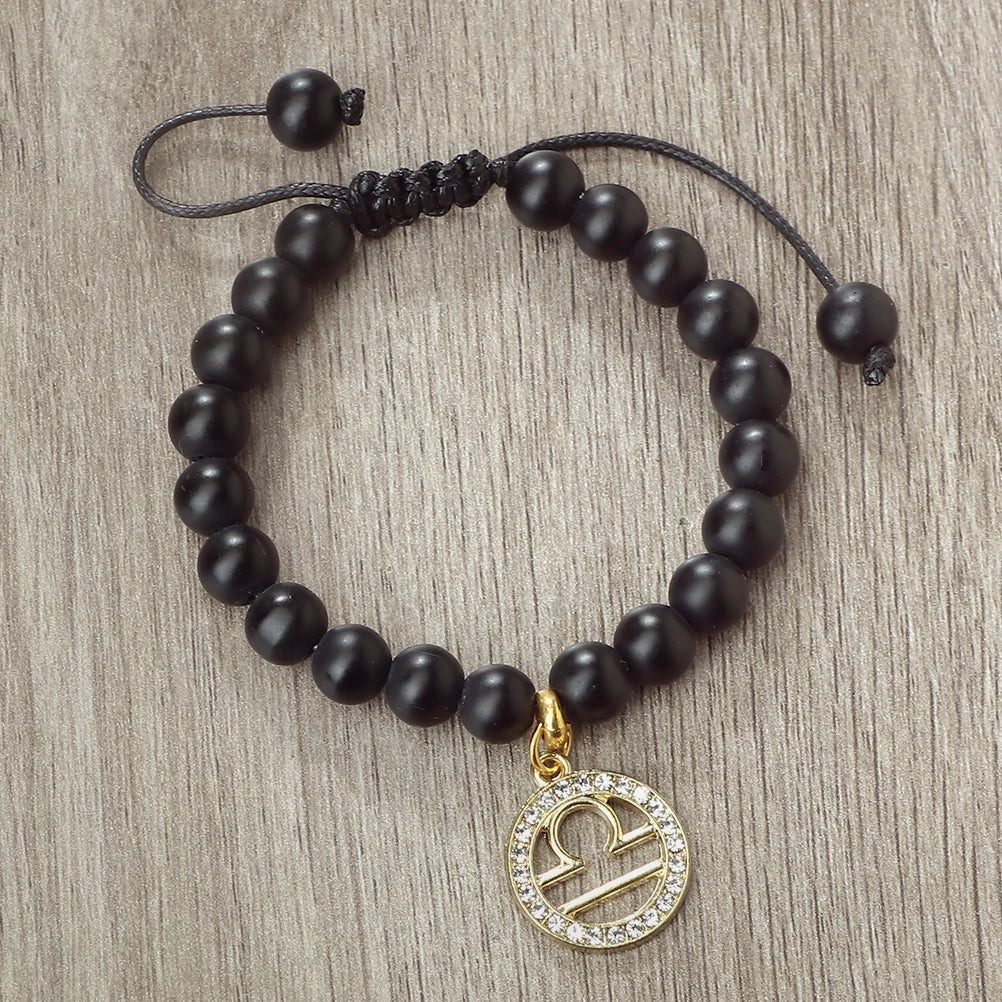 A black beaded bracelet with a gold charm featuring the zodiac symbol for Libra.