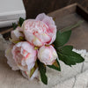 A bouquet of elegant artificial silk peonies in shades of pink and white resting on a beige linen cloth.
