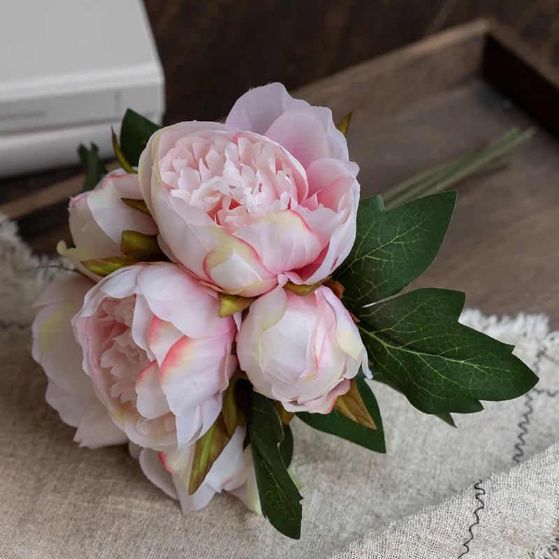 A bouquet of elegant artificial silk peonies in shades of pink and white resting on a beige linen cloth.