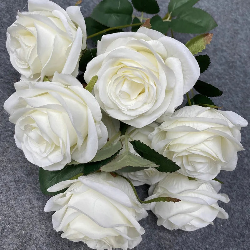 A bouquet of nine realistic white silk roses arranged on a dark gray background.