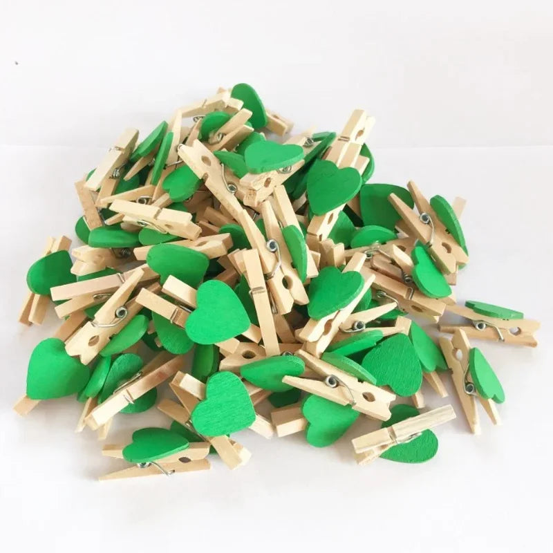 A pile of small, heart-shaped wooden photo clips in light wood and green are scattered on a white surface.