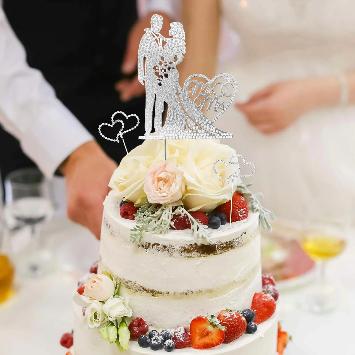 A tiered white wedding cake decorated with crystal embellished Mr and Mrs toppers and fresh flowers.